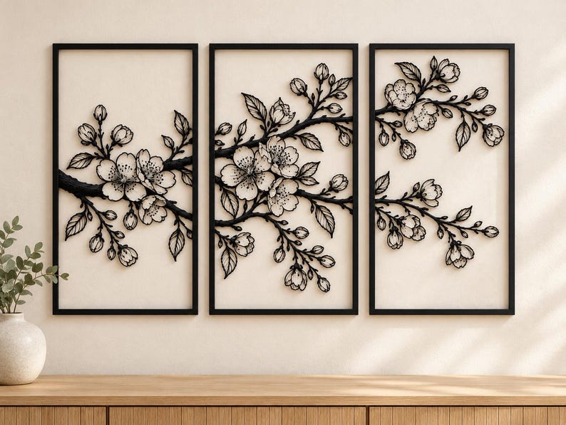 May include: A triptych wall art set featuring three rectangular black frames. Each frame contains a black metal cutout of cherry blossom branches with detailed flowers, buds, and leaves, creating a continuous floral design across the panels.