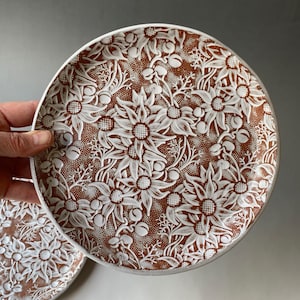 May include: Two decorative plates with a floral design. The plates have a raised white floral design on a brown background. The rims are white. The plates are round and appear to be ceramic.