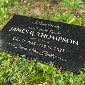 May include: A black granite memorial plaque with white engraved text. The inscription reads "In Loving Memory" above "JAMES R. THOMPSON" and dates "OCT 15, 1945 - FEB 14, 2025". The phrase "Forever in Our Hearts" is at the bottom.