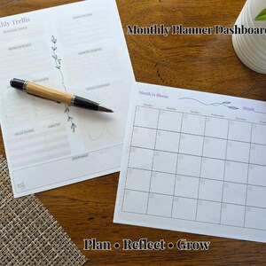 May include: Two white paper planner dashboards with the text "Monthly Trellis" and "Month in bloom" on a wooden surface. A pen with a wooden barrel rests on the left planner. The text "Plan • Reflect • Grow" is at the bottom.