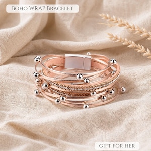 May include: A multi-strand wrap bracelet featuring metallic rose gold leather cords, a central row of clear rhinestones, and small silver-toned metal beads. The bracelet includes a rectangular magnetic clasp and displays the text BOHO WRAP BRACELET and GIFT FOR HER.