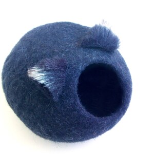May include: A dark blue felt cat bed with a round opening and two fuzzy ears.