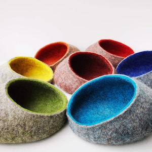 May include: A set of seven felted wool bowls in various colors, including gray, green, blue, yellow, and red. The bowls are all round and have a smooth, soft texture.