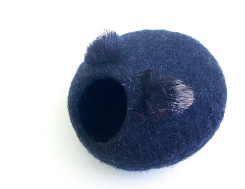 May include: A dark blue felt nesting ball with a small black and white fur pom-pom on top.