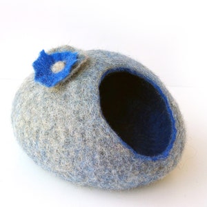 K&ouml;nnte beinhalten: Ein graues und blaues Filztierbett in Form einer H&ouml;hle mit einer blauen Filzblume oben drauf.