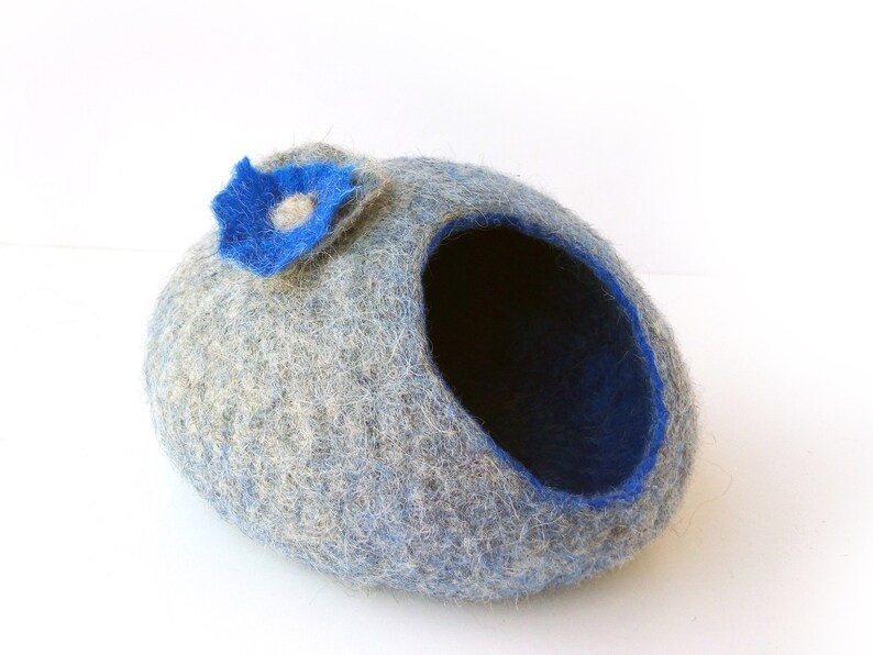 K&ouml;nnte beinhalten: Ein graues und blaues Filztierbett in Form einer H&ouml;hle mit einer blauen Filzblume oben drauf.