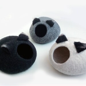 May include: Three felt pet beds in gray, black, and white. Each bed has a round shape with a hole in the center for a pet to enter. The beds have black felt ears on the top.