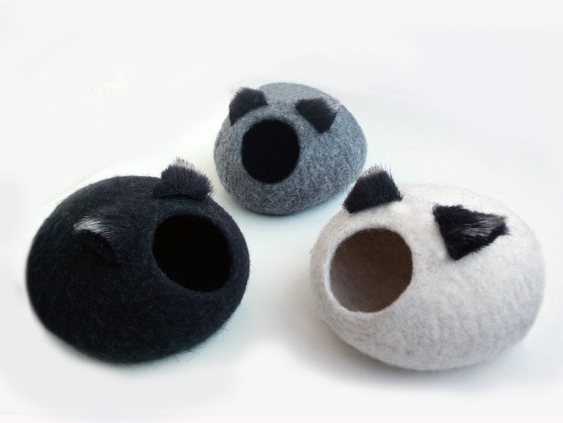 May include: Three felt pet beds in gray, black, and white. Each bed has a round shape with a hole in the center for a pet to enter. The beds have black felt ears on the top.