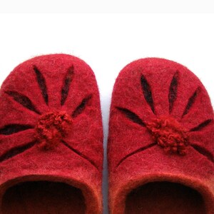 May include: A pair of red wool slippers with a flower design. The slippers have a dark red trim around the edges and a small pom-pom in the center of each flower.