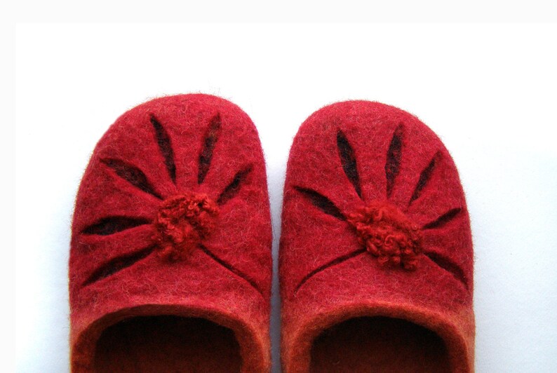May include: A pair of red wool slippers with a flower design. The slippers have a dark red trim around the edges and a small pom-pom in the center of each flower.