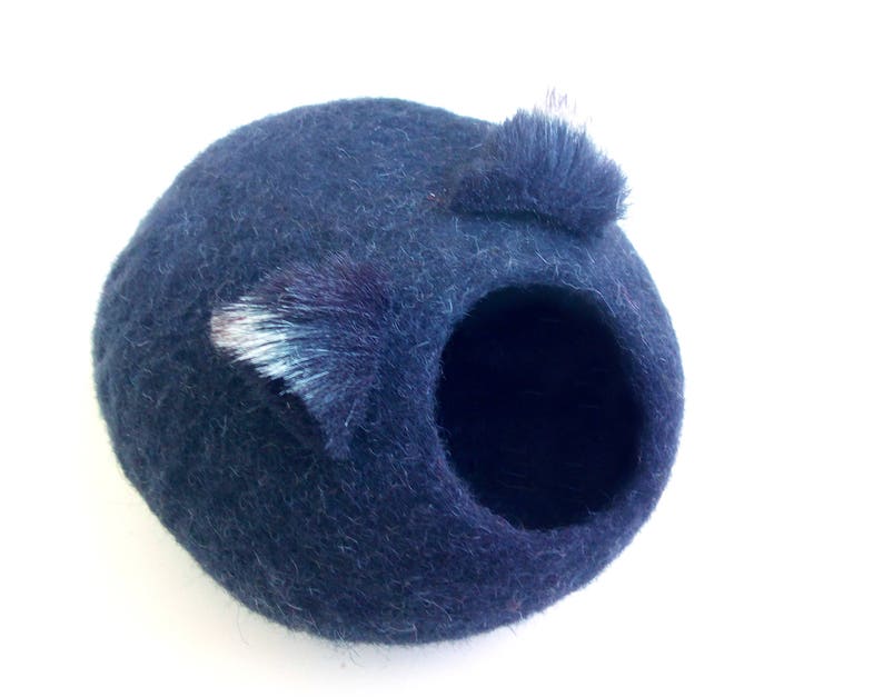 May include: A dark blue felt cat bed with a round opening and two fuzzy ears.