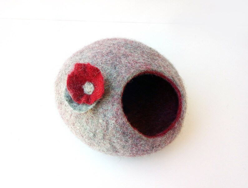 May include: A gray and red felt pet bed with a red flower on the side. The bed has a round opening for the pet to enter.