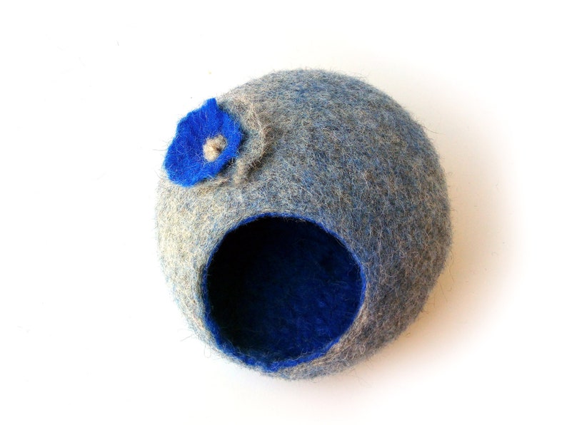 K&ouml;nnte beinhalten: Ein blaues und graues Filztierbett mit einer blauen Filzblume an der Seite. Das Bett hat eine runde &Ouml;ffnung, durch die das Tier hineinkommt.