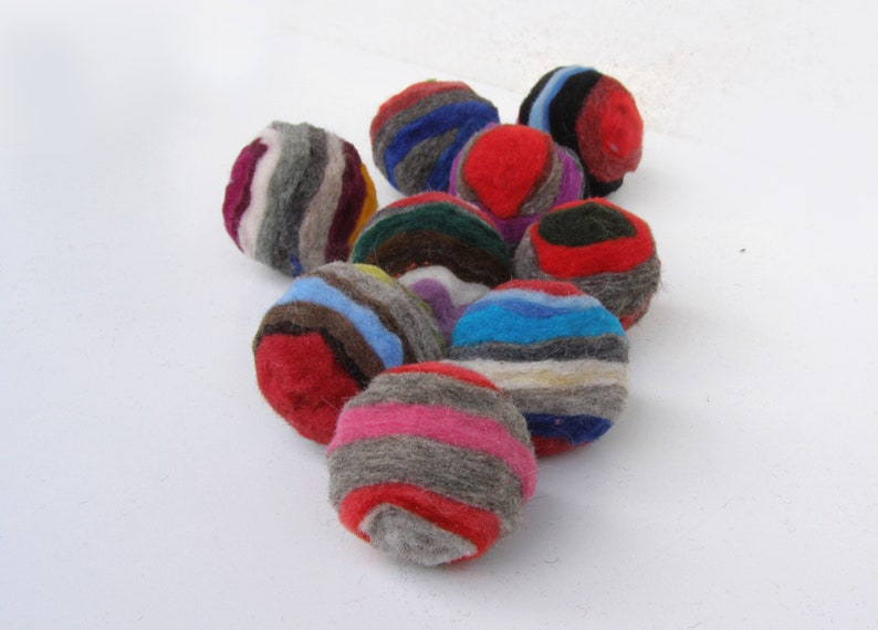 K&ouml;nnte beinhalten: Eine Sammlung bunter, gestreifter Filzkugeln. Die Kugeln sind aus Wolle und haben einen Durchmesser von etwa 5 cm. Sie sind perfekt, um jedem Raum einen Hauch von Farbe und Textur zu verleihen.