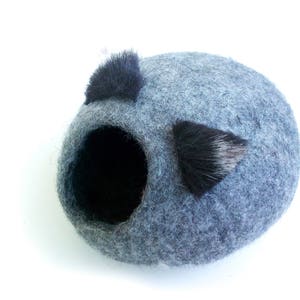 May include: A gray felt cat bed with two black fur ear-like accents. The bed has a round opening for the cat to enter.