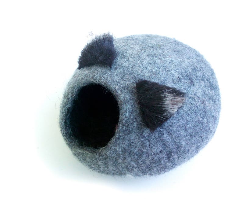 May include: A gray felt cat bed with two black fur ear-like accents. The bed has a round opening for the cat to enter.