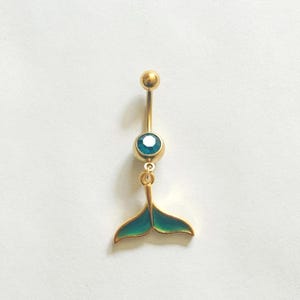 Può includere: Gioiello per il corpo in oro con una gemma blu e un ciondolo a forma di coda di sirena.