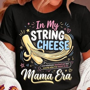 Könnte beinhalten: Schwarzes T-Shirt mit dem Text "In My String Cheese Mama Era" in verspielter Schrift. Das Design beinhaltet eine Illustration von Käsefäden und den Satz "overwhelmed, touched out but exactly who I'm meant to be."