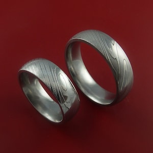 May include: Two silver wedding bands with a unique patterned design. The bands are made of metal and have a brushed finish.