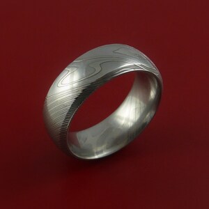 May include: A silver ring with a patterned design. The ring is made of metal and has a smooth, polished finish.