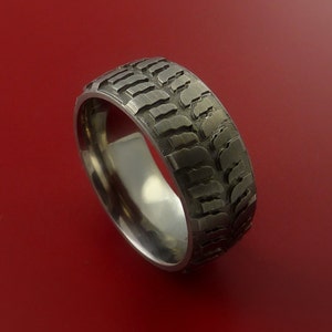 May include: A silver titanium ring with a tire tread pattern. The ring is a unique and stylish accessory for anyone who loves off-roading.
