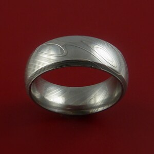May include: A silver ring with a unique patterned design. The ring is made of metal and has a smooth, polished finish.