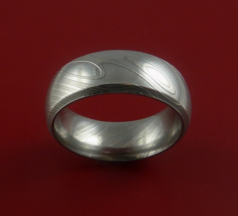 May include: A silver ring with a unique patterned design. The ring is made of metal and has a smooth, polished finish.