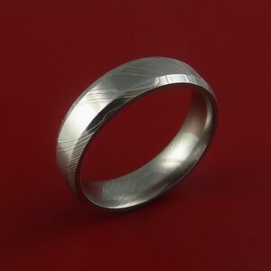 May include: A silver-toned wedding band with a unique, patterned design. The band is made of Damascus steel and has a polished finish.