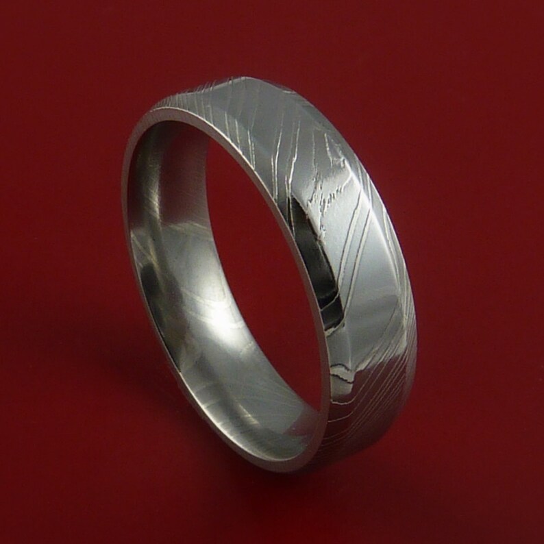 May include: A silver-toned wedding band with a unique, textured, patterned design. The band is made of metal and has a polished finish.