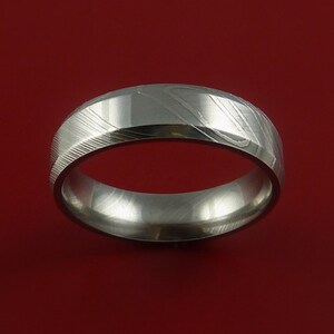 May include: A silver-coloured wedding band with a brushed finish and a unique pattern. The band is made of metal and has a rounded shape.
