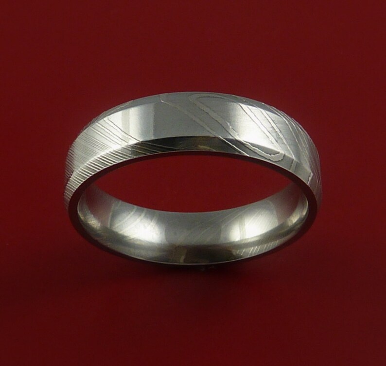May include: A silver-coloured wedding band with a brushed finish and a unique pattern. The band is made of metal and has a rounded shape.