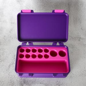 May include: Open purple and pink plastic storage case. The case has a hinged lid with pink clasps. Inside, a pink tray features various circular compartments and a rectangular section, designed for organizing small items.