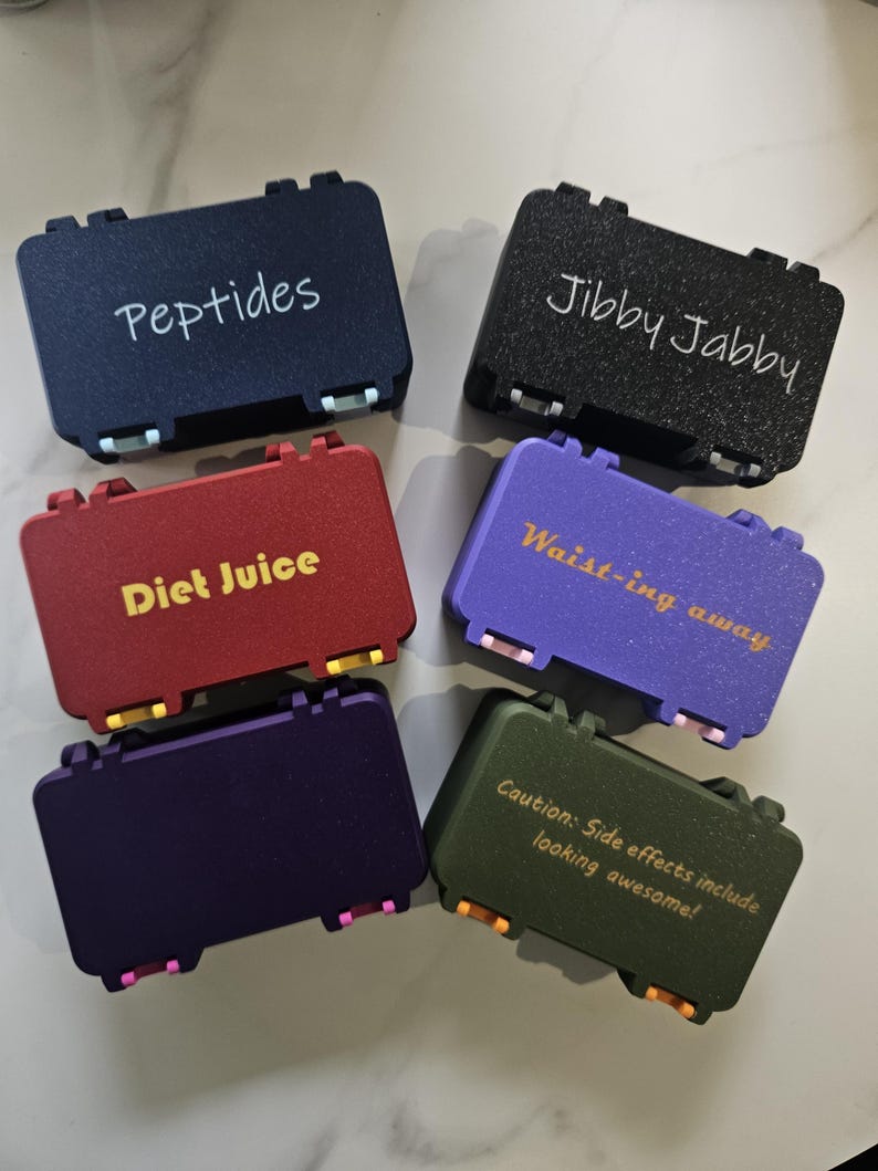 May include: Six small, colorful cases with hinged lids. Each case has text on the top: "Peptides", "Jibby Jabby", "Diet Juice", "Waist-ing away", and "Caution: Side effects include looking awesome!". The cases are navy, black, red, purple, dark purple, and olive green.
