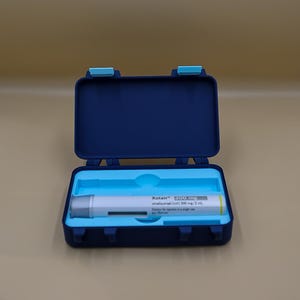 Peut inclure: Un étui rectangulaire en plastique bleu foncé avec un plateau intérieur bleu clair contenant un stylo prérempli blanc Xolair 300 mg. L'étiquette indique Xolair 300 mg, omalizumab (rsh) 300 mg/2 mL, solution injectable en stylo prérempli.