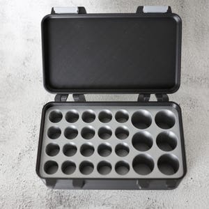 May include: Open black plastic storage case with a gray interior featuring multiple circular compartments. The case has a hinged lid with gray latches, designed for organizing small items.