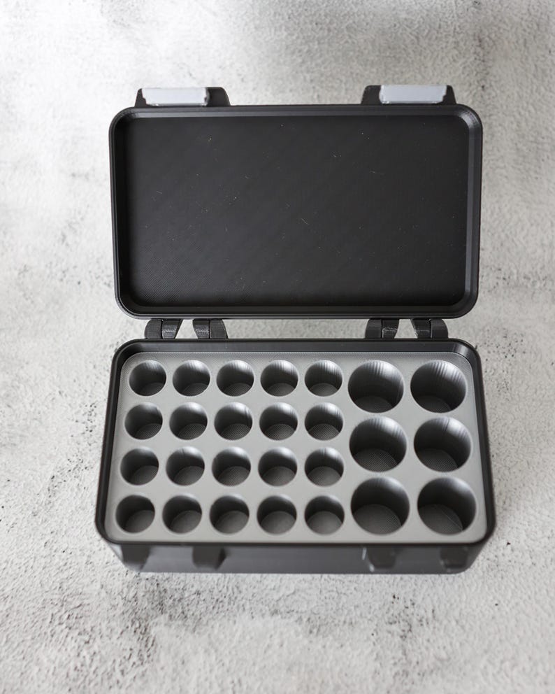 May include: Open black plastic storage case with a gray interior featuring multiple circular compartments. The case has a hinged lid with gray latches, designed for organizing small items.