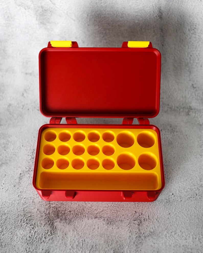 May include: Open red toolbox with yellow interior and compartments. The toolbox is rectangular with a hinged lid and yellow latches. The interior has multiple circular compartments and a long rectangular compartment.
