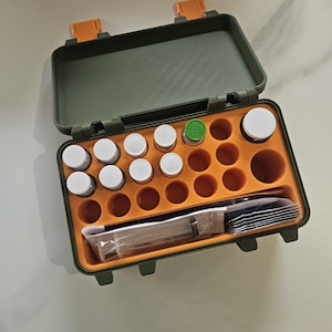 May include: Open, olive green and orange medical kit with a variety of small white-capped bottles, a syringe, and other medical supplies. The kit has an orange interior with circular compartments for the bottles and a section for the syringe and other items.