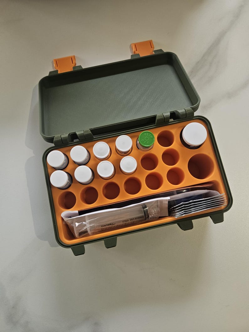 May include: Open, olive green and orange medical kit with a variety of small white-capped bottles, a syringe, and other medical supplies. The kit has an orange interior with circular compartments for the bottles and a section for the syringe and other items.