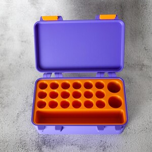 May include: Open purple plastic toolbox with orange interior. The toolbox has a rectangular shape with a hinged lid and orange latches. The interior features multiple circular compartments and a rectangular slot.