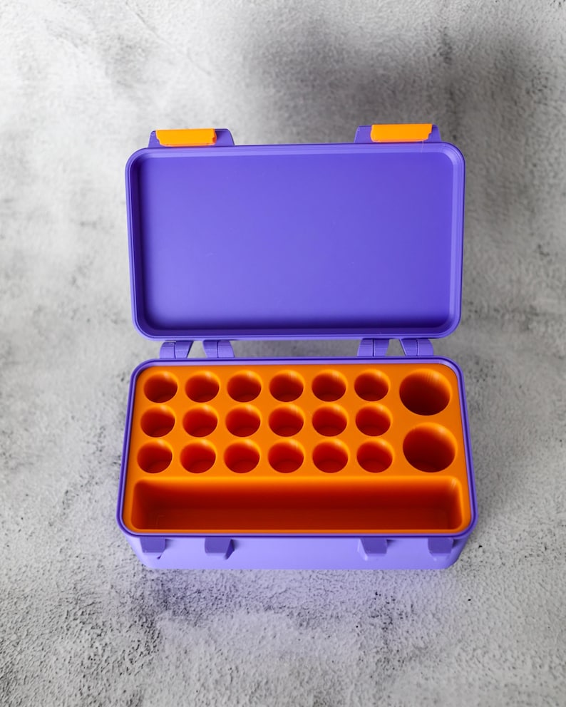May include: Open purple plastic toolbox with orange interior. The toolbox has a rectangular shape with a hinged lid and orange latches. The interior features multiple circular compartments and a rectangular slot.