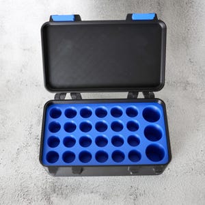 May include: An open black plastic case with a blue interior. The case has a rectangular shape with a hinged lid and blue clasps. The interior has multiple circular compartments of varying sizes.