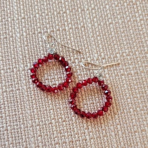 May include: A pair of red crystal earrings with silver hooks. The earrings are made of small, round crystals that are strung together to form a circle.