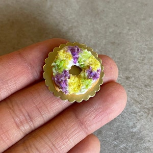 May include: A miniature King Cake replica with purple, green, and gold icing on a gold-colored base.