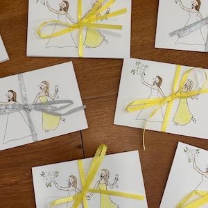 Puede incluir: Una colecci&oacute;n de tarjetas rectangulares blancas con un dibujo lineal de dos figuras con vestidos, una sosteniendo un ramo y la otra una copa. Algunas tarjetas est&aacute;n atadas con cinta amarilla brillante, otras con cinta plateada.