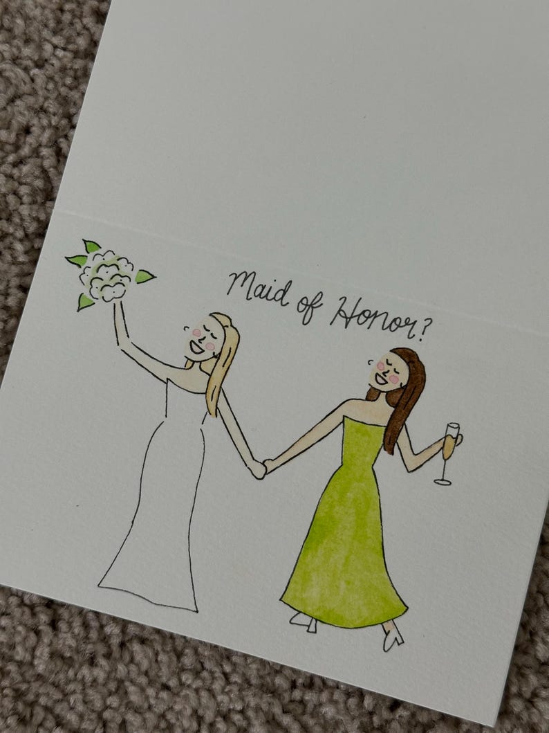 Puede incluir: Una tarjeta de felicitaci&oacute;n blanca con una ilustraci&oacute;n dibujada a mano de dos figuras tomadas de la mano. Una figura lleva un vestido blanco y sostiene un ramo, mientras que la otra lleva un vestido verde y sostiene una copa. El texto Maid of Honor? aparece arriba.