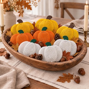 May include: A collection of decorative pumpkins crafted from a yellow, orange, and white mesh material, each featuring a solid-colored stem. These pumpkins are arranged inside a large, oval-shaped wooden bowl alongside scattered brown acorns and leaves.