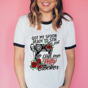 May include: White t-shirt with a black ringer, featuring a black and white illustration of a sewing machine with a red rose and the text "Got my spoon ready to stir the pot so call me Petty Crocker".