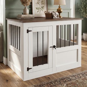 Op de afbeelding: Een witte houten hondenbench met een donkerbruin bovenoppervlak, voorzien van verticale zwarte metalen spijlen aan de zijkanten en een voordeur met zwarte metalen scharnieren en een grendel. De structuur heeft een rechthoekig frame en een stevige bodem.