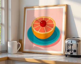 May include: A framed art print featuring a stylized illustration of a grapefruit half with a cherry on top, resting on a teal plate against a pink background. The artwork is in a wooden frame, displayed on a countertop with a white mug and a chrome toaster.